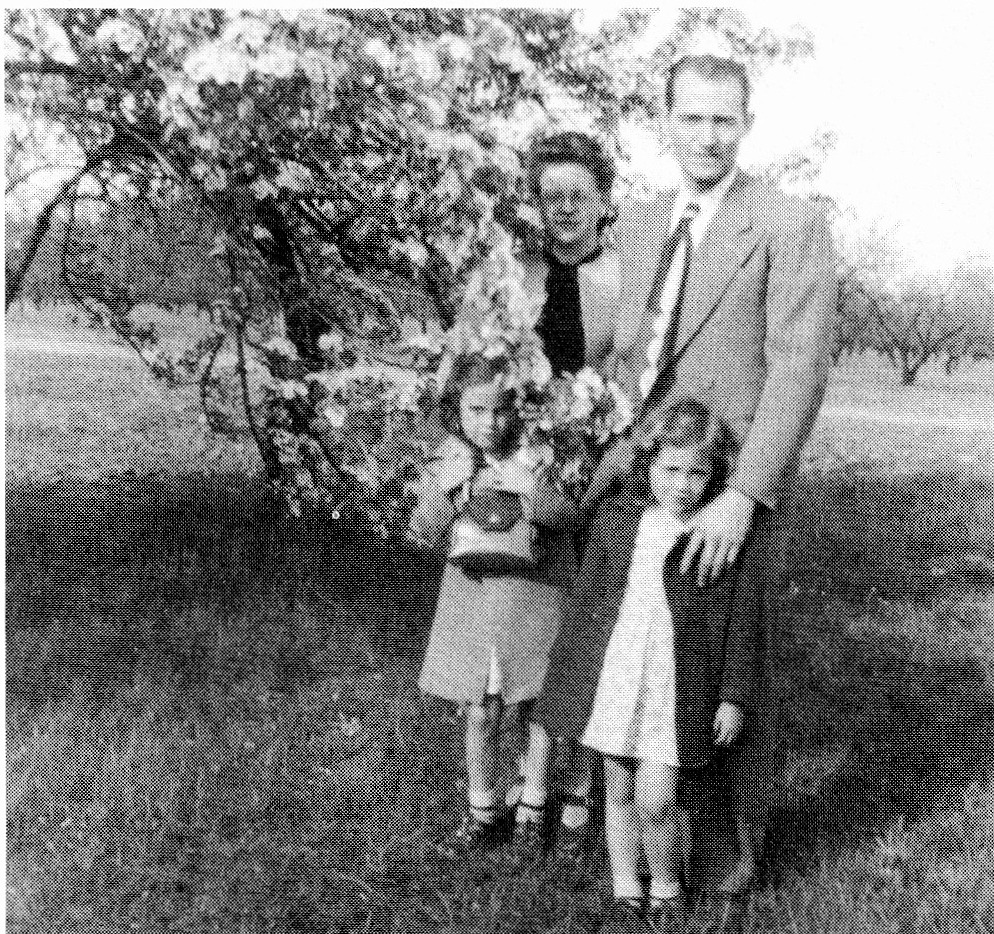Black and white photograph of a family of four standing outdoors in front of trees.