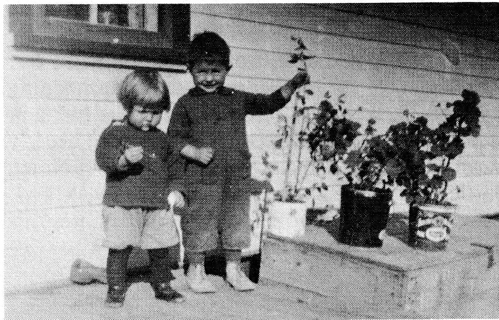 Two young children, a boy and a girl, playing outdoors near a house.
