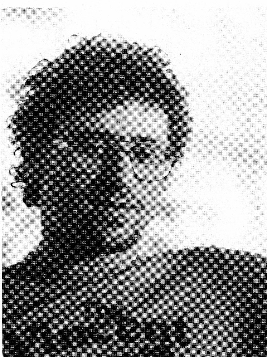 Young man with glasses and curly hair wearing a 'The Vincent' shirt