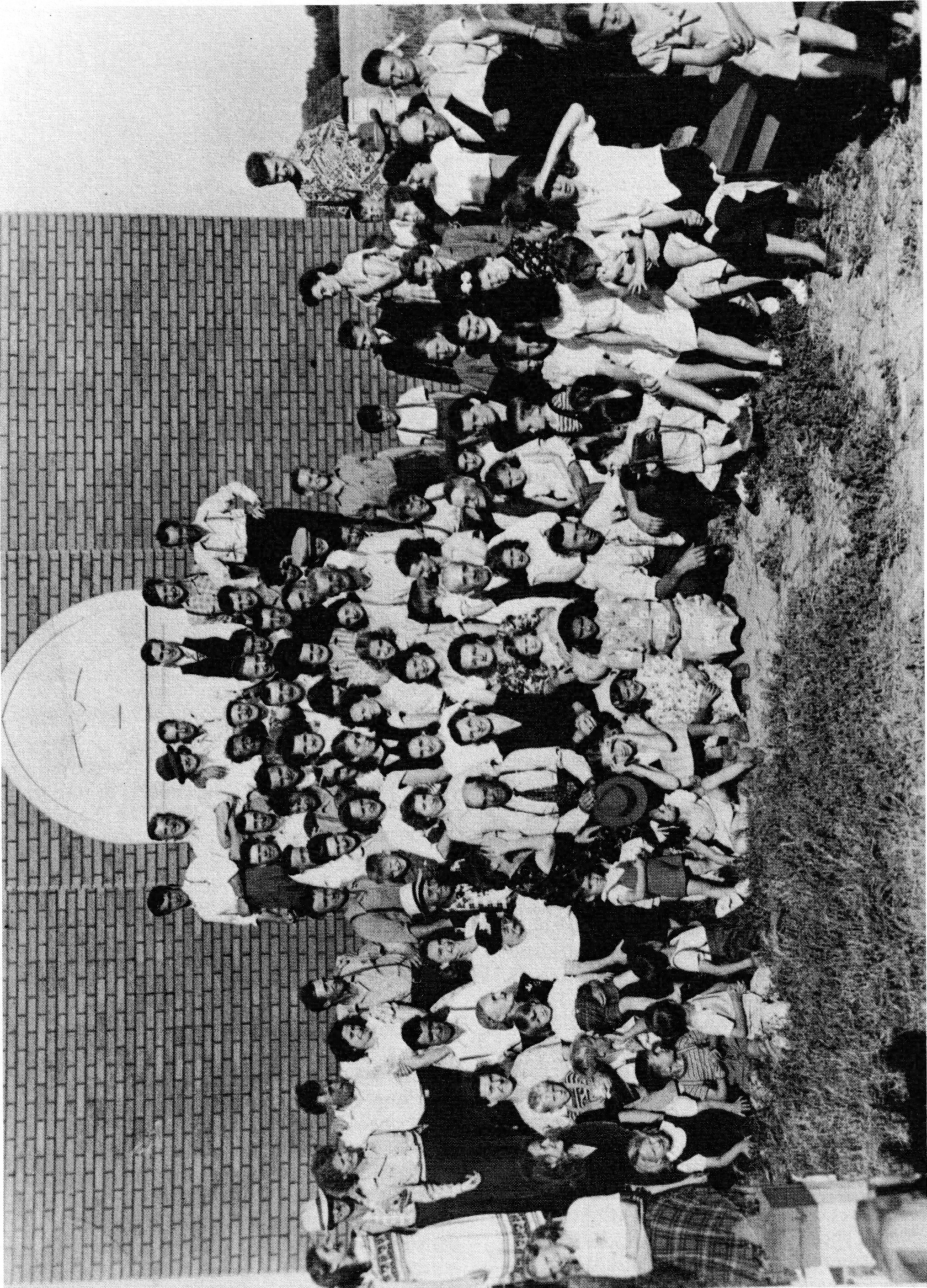 Large group of people gathered for a picnic in front of a brick building